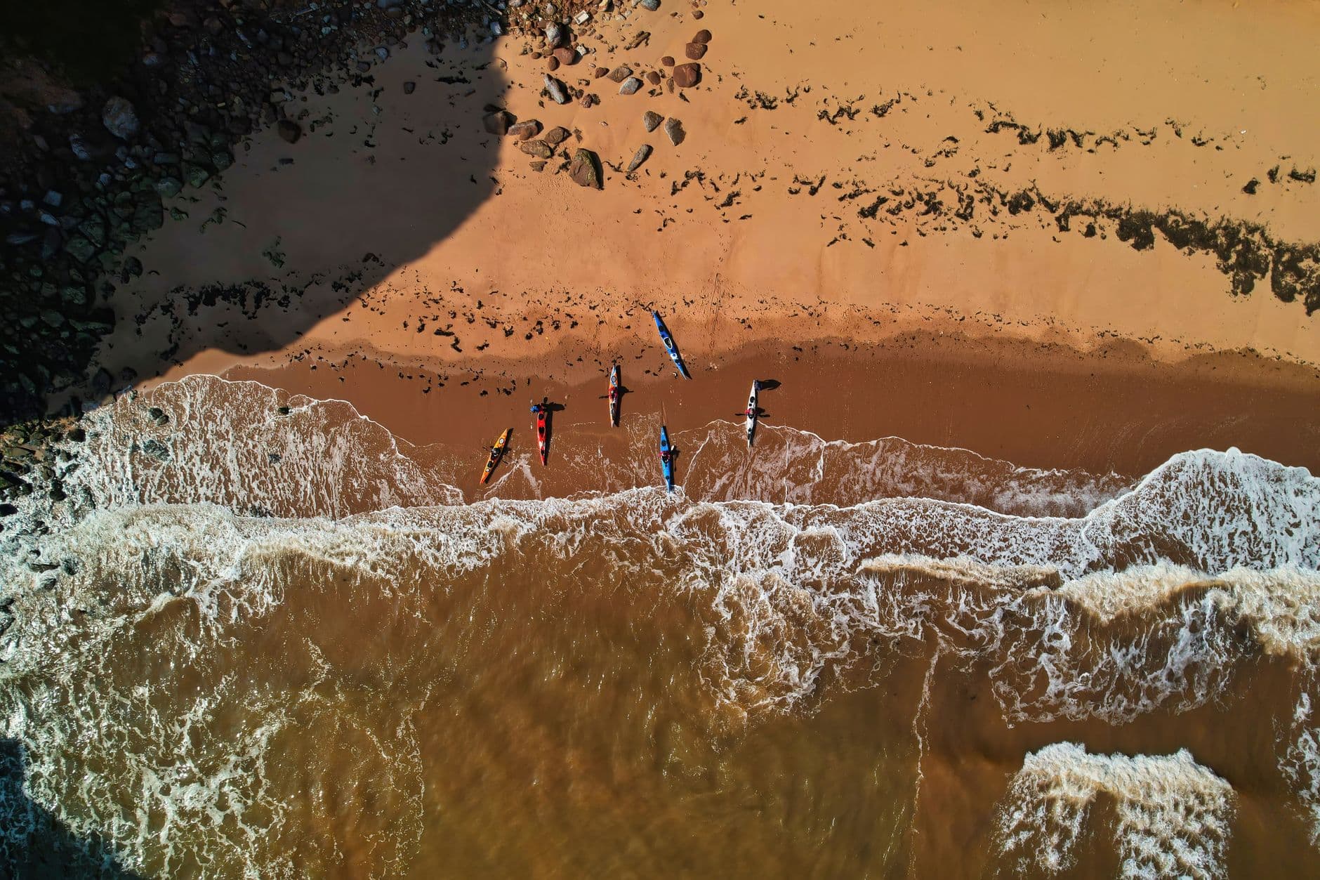 Kayaks lined up on a sandy shore with small waves running in behind them.